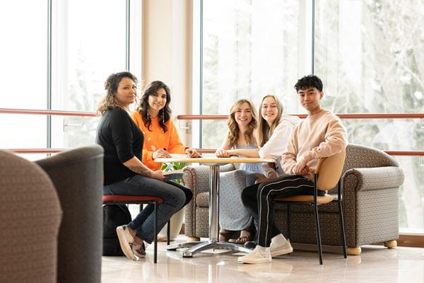 Five studies sitting at a table smiling at the camera. 