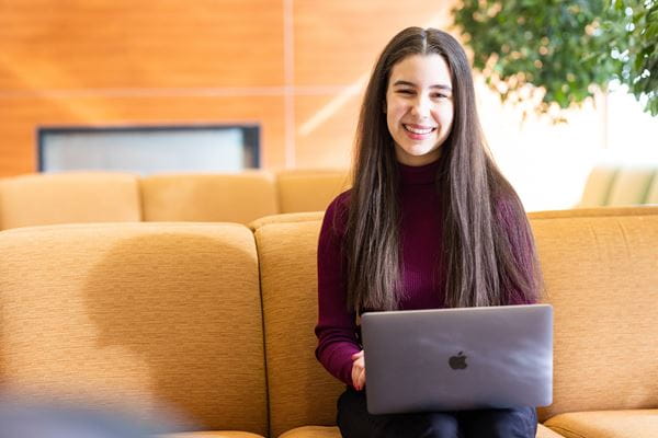 Student studying on tan couch with a laptop.