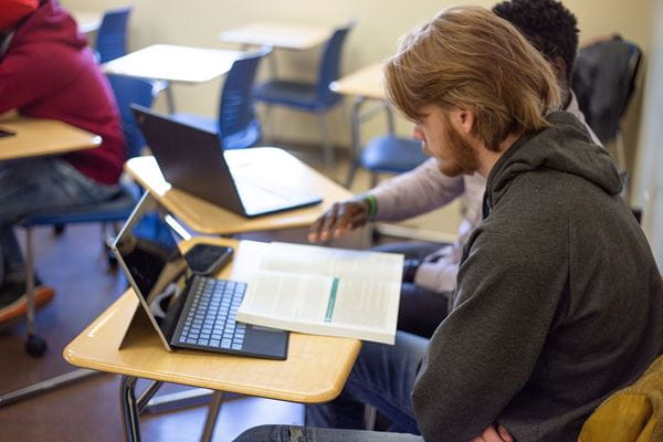 Students reading and using laptop in classroom.