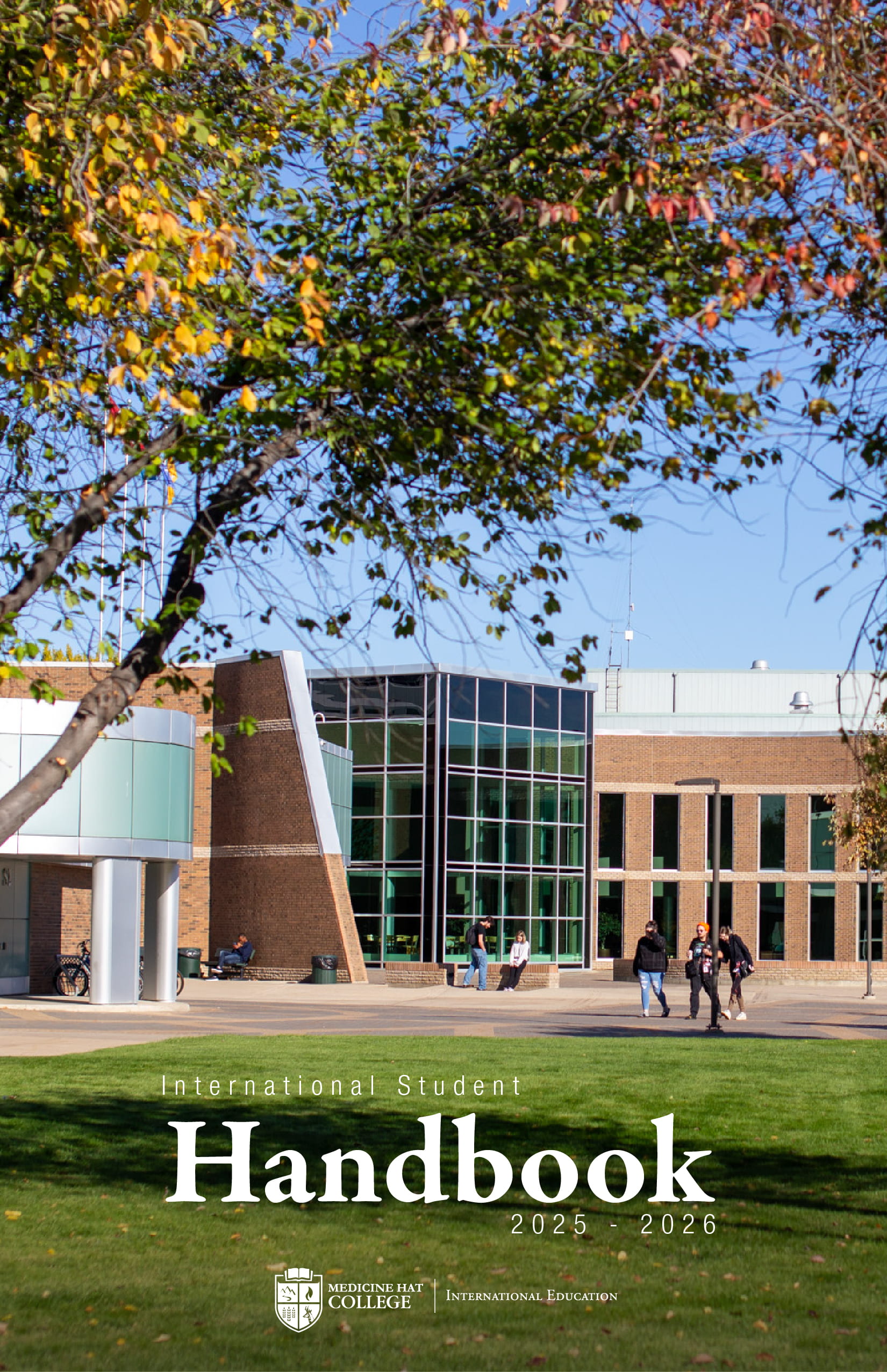 Front cover of the International Handbook. Behind the orange, green, and yellow leaves from a tree is the entrance the MHC campus with students walking among the grounds.