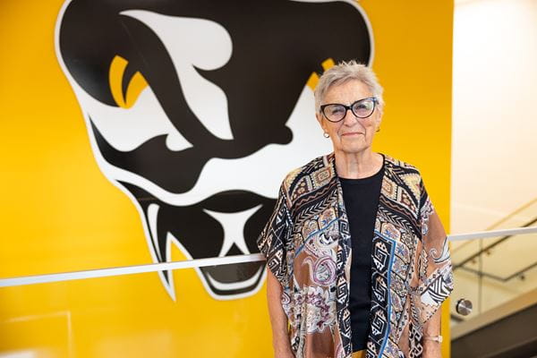 Alumni and former student-athlete from 1965 stands in front of a yellow wall with the Rattlers logo, an addition made with the new fitness centre.