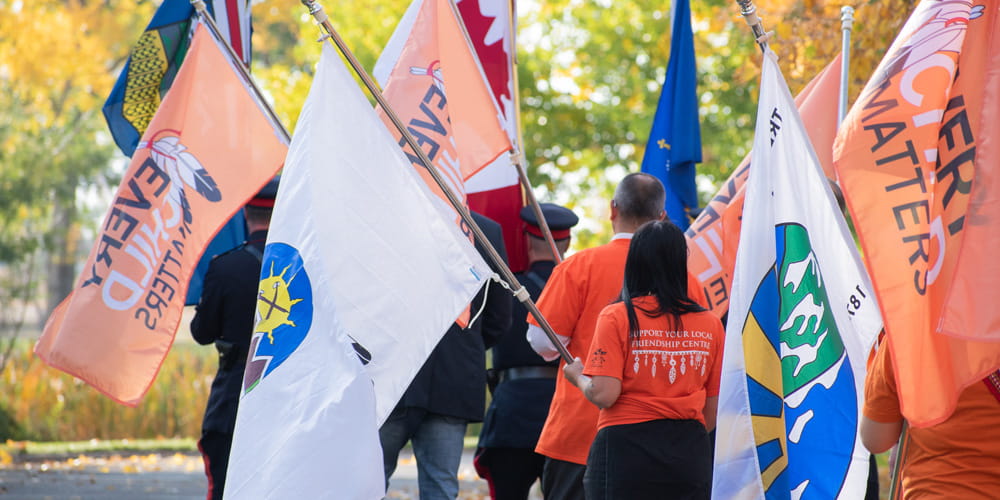 Community members walk together holding flags on National Day for Truth & Reconciliation