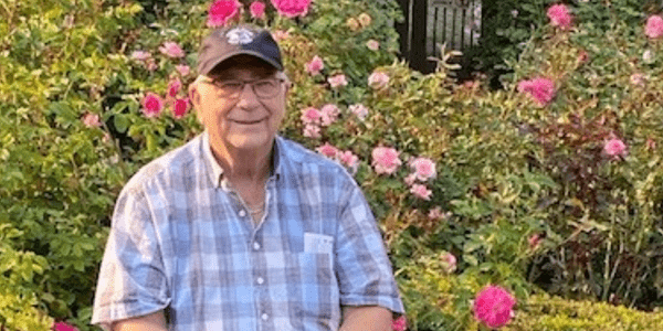 Keith Elhart seated in front of a bush of flowers.
