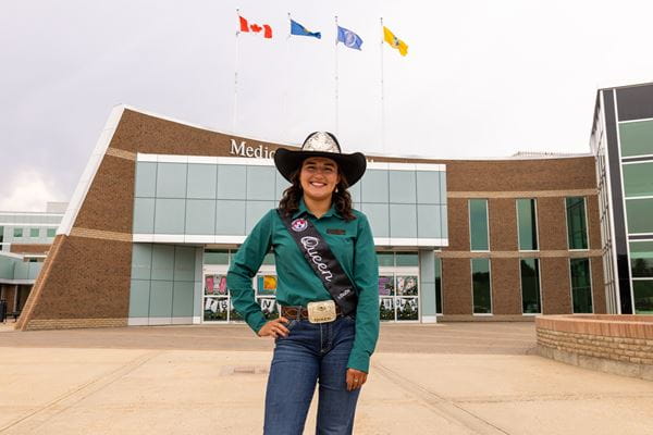 Woman in cowboy hat in green shirt stands outside of brick building.
